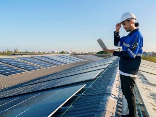 Engineer in a hard hat holding a laptop while inspecting a commercial rooftop solar array