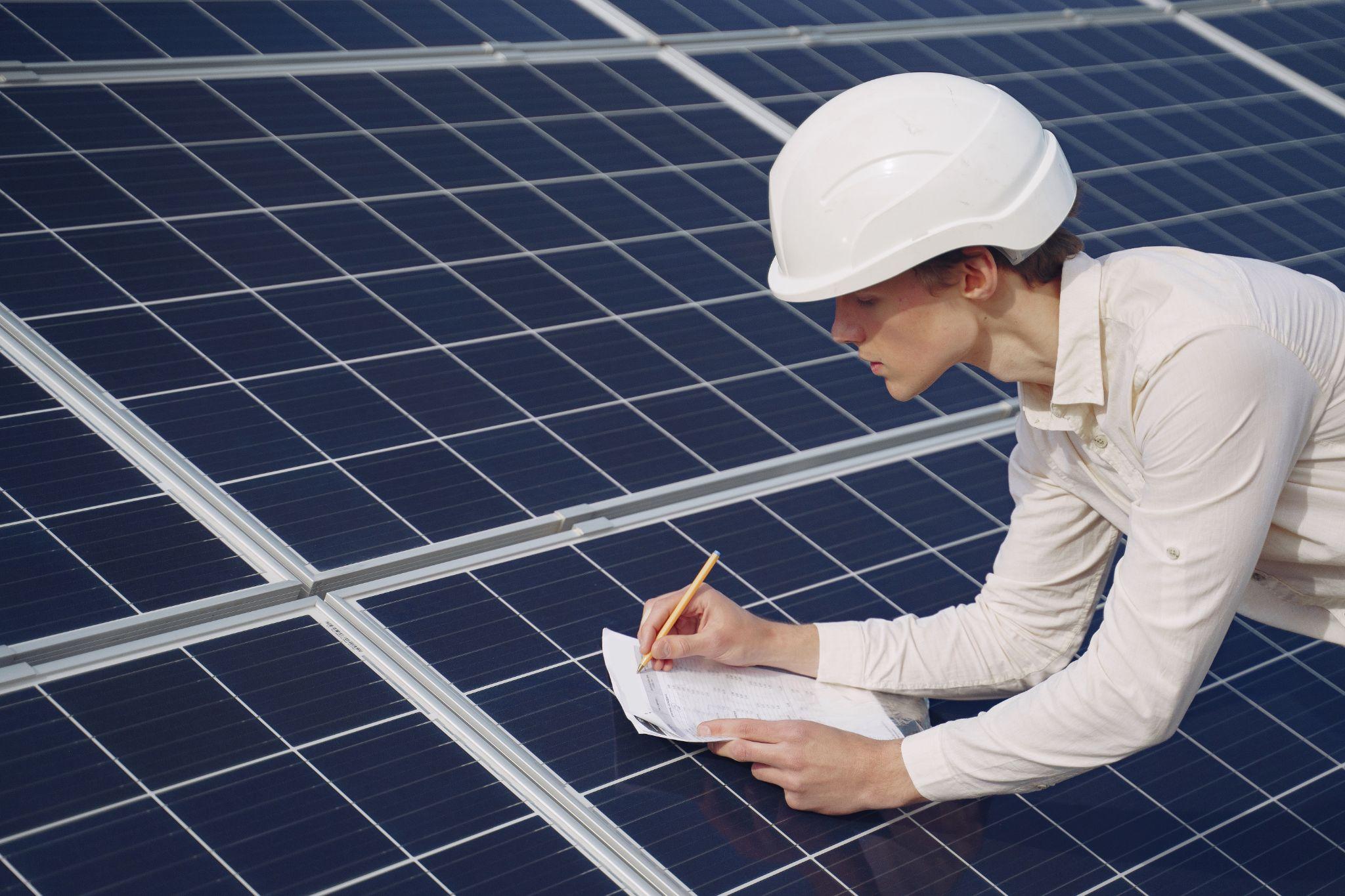 An engineer in a hard hat noting readings on a row of solar panels