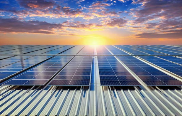 Rows of solar panels on a corrugated metal roof with the sun setting behind them