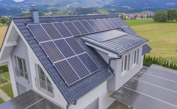Aerial view of a two-storey house with rooftop solar panels, surrounded by green fields