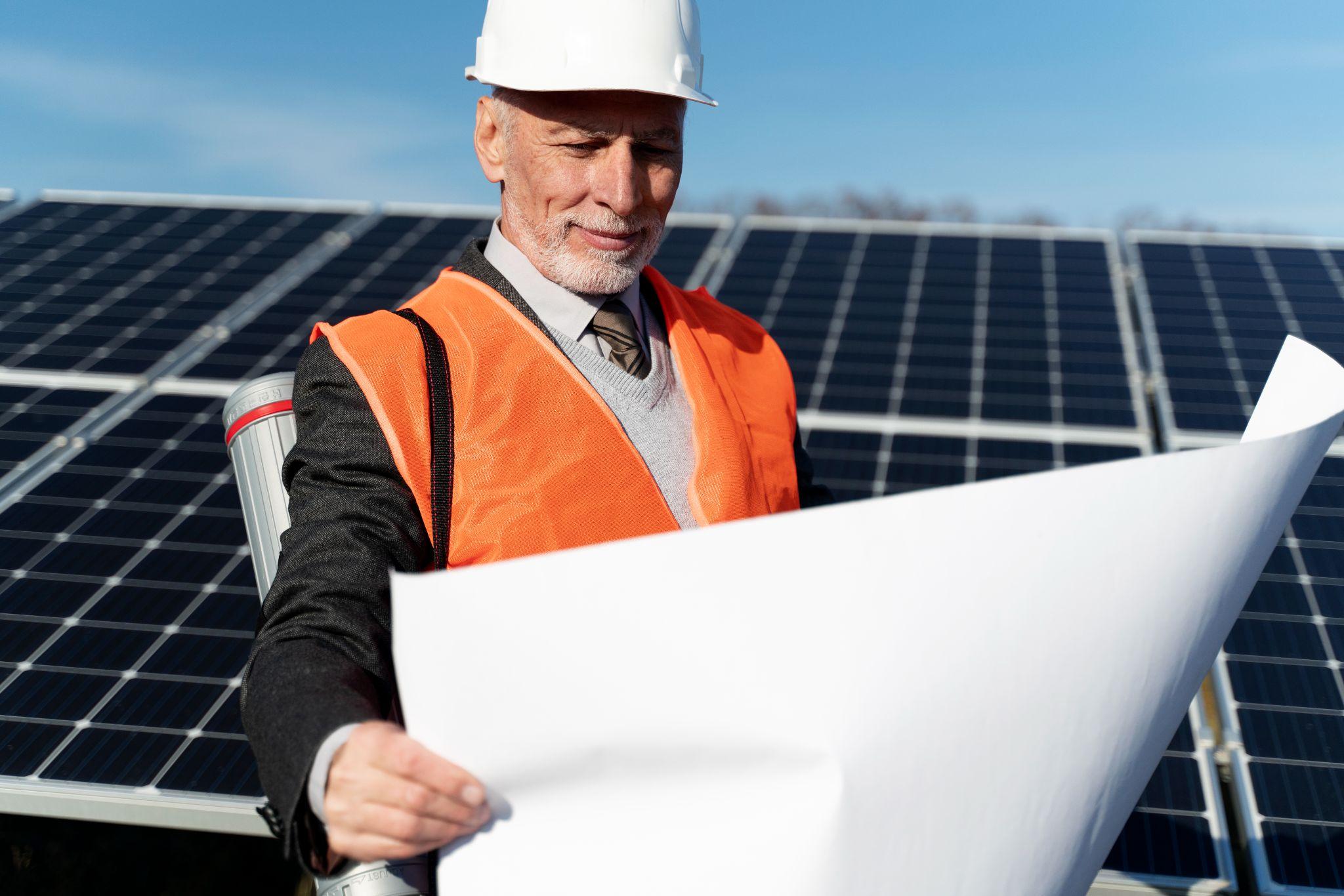 An engineer in a hi-vis vest reviewing plans in front of a ground-mounted solar array