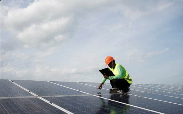 Technician in a hard hat kneeling on a solar array, checking the panels with a tablet