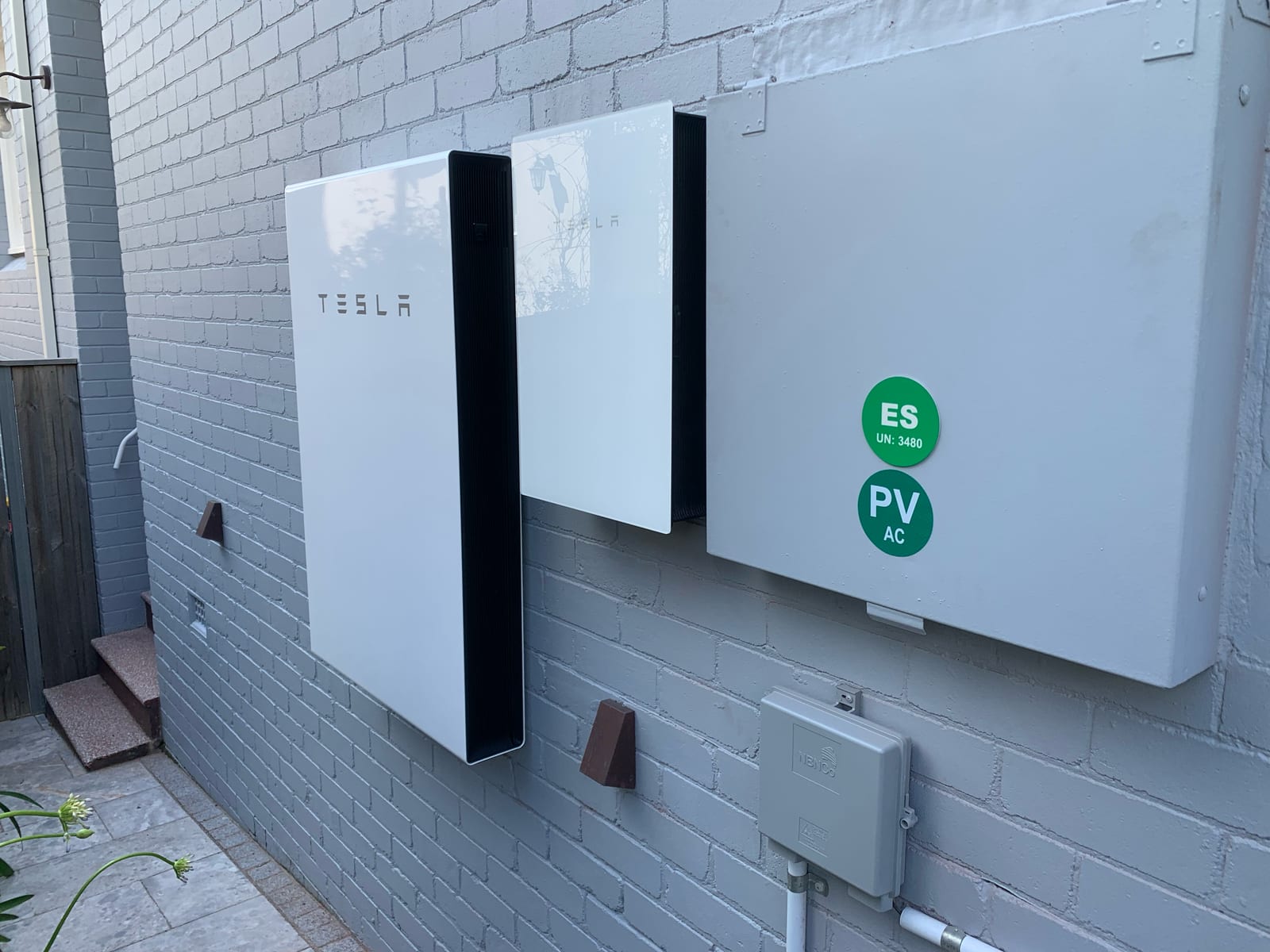 Two Tesla Powerwall batteries installed beside the switchboard on a painted brick wall