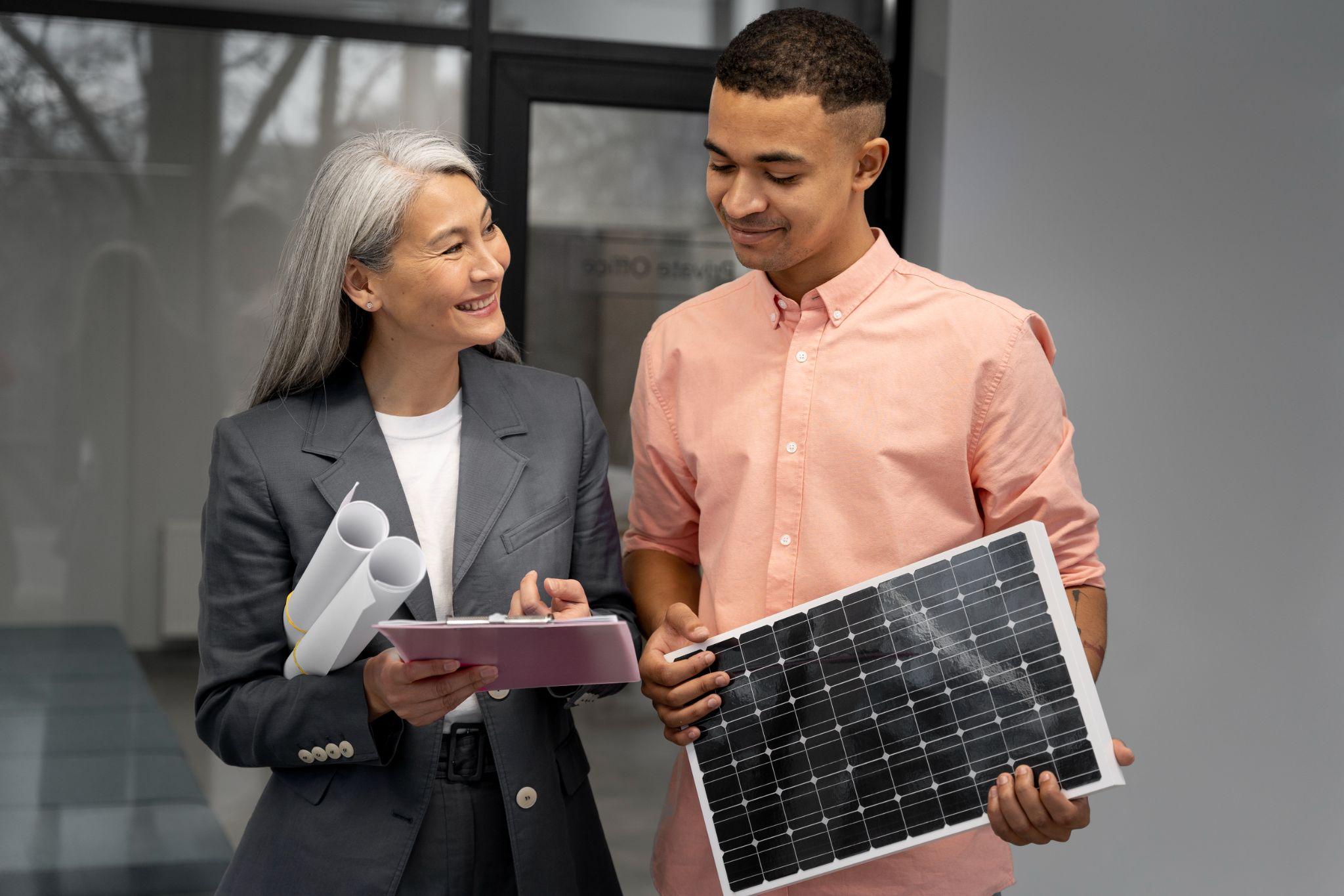 A consultant holding plans and a clipboard beside a homeowner holding a solar panel
